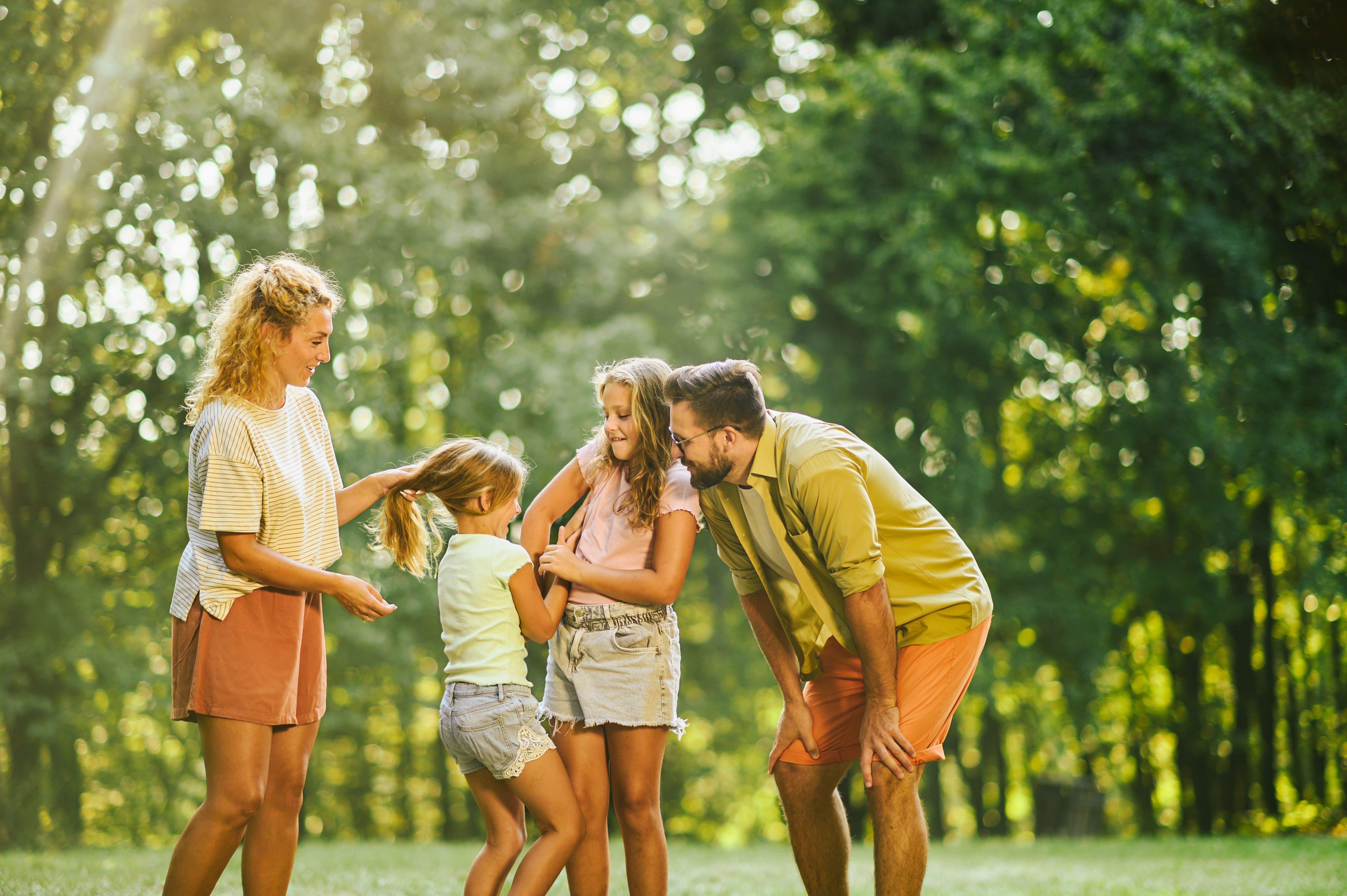 Família se divertindo em uma área verde, com os pais assistindo as filhas brincarem.