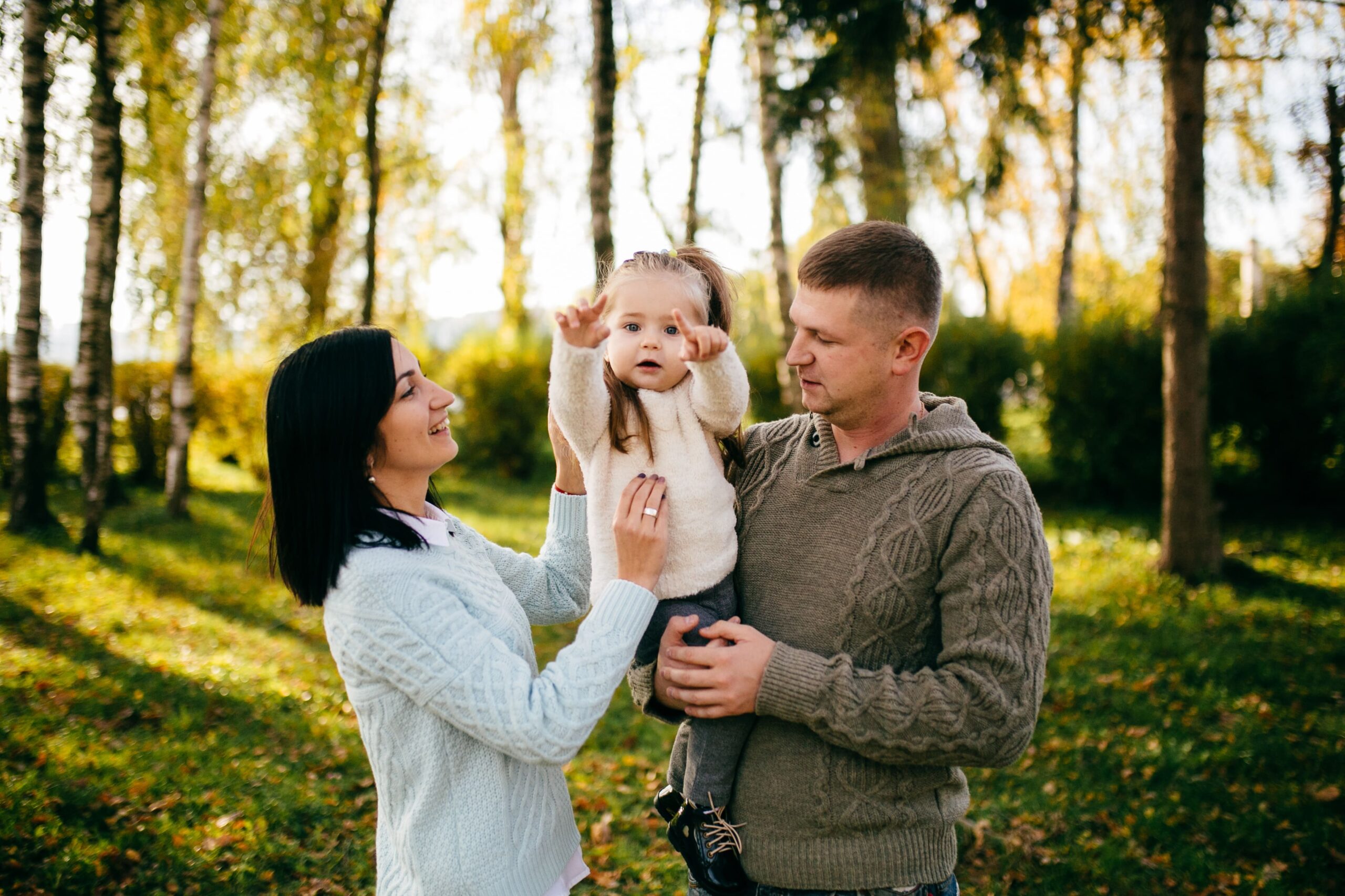 Família feliz com pai, mãe e filha pequena brincando juntos na natureza durante um dia ensolarado.